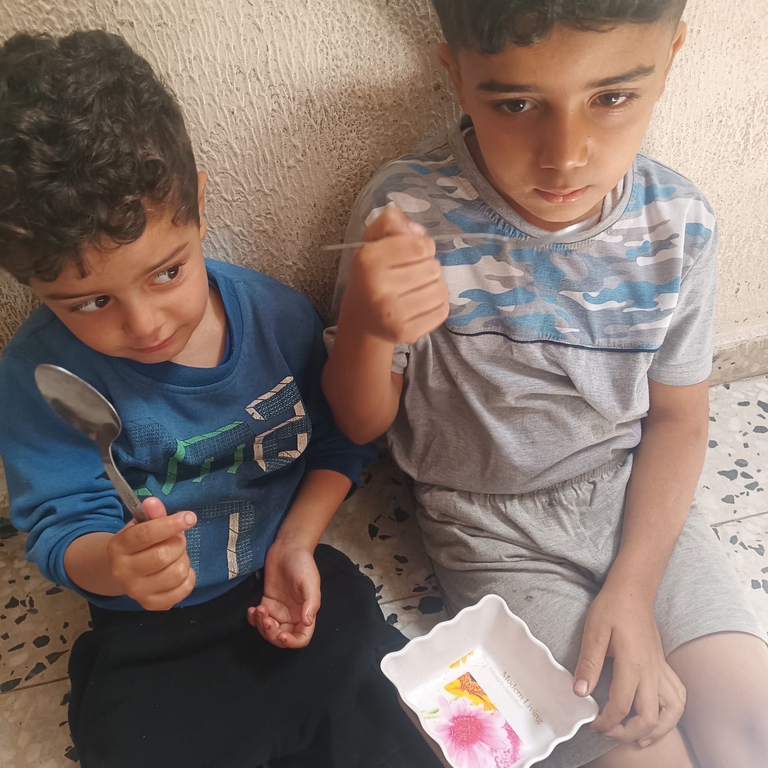 Courtesy of Tariq’s family. Two children holding spoons and an empty dish; image for Help Gaza family evacuate.
