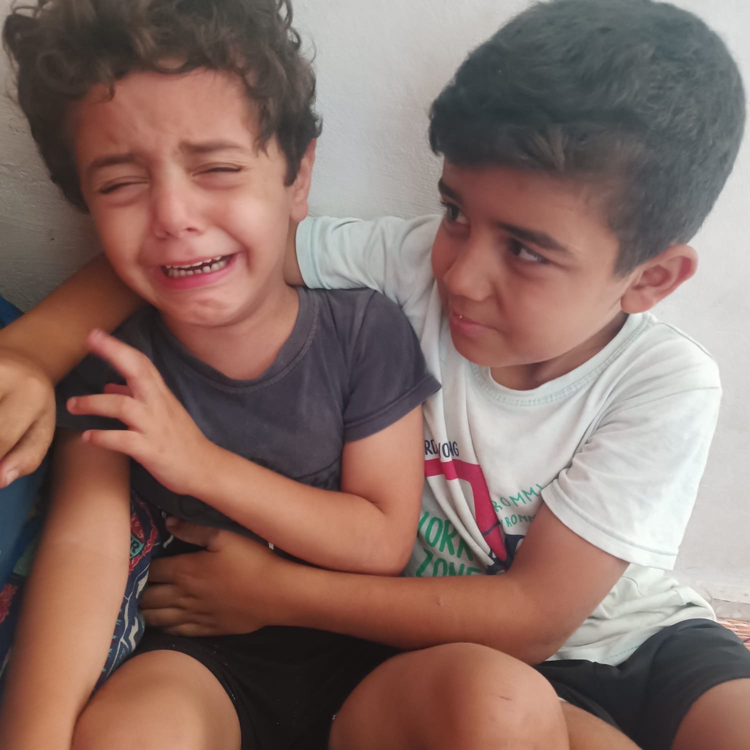 Courtesy of Tariq’s family. Jude crying while Musa comforts him in Gaza shelter; Help Gaza family evacuate.