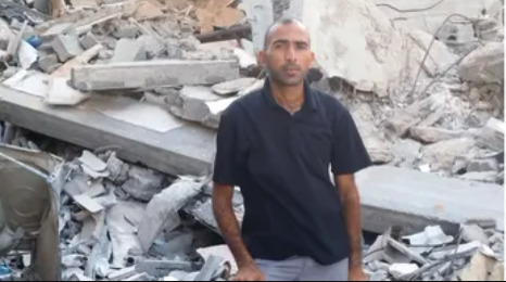 Gaza teacher displaced, standing in rubble of his destroyed home with family.