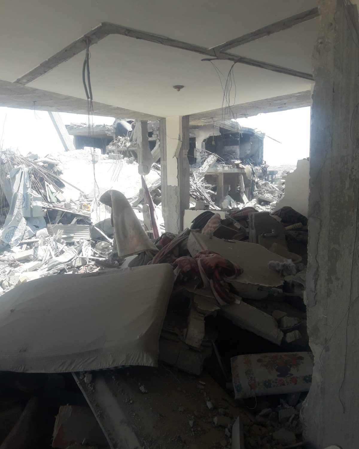 Rubble and collapsed concrete near a temporary shelter; illustrates destroyed housing and urgent shelter needs for Gaza family emergency aid.
