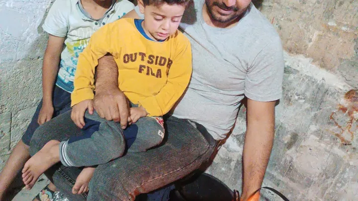 Courtesy of Tariq’s family. Tariq sitting with his two young sons in harsh shelter conditions; Help Gaza family evacuate.